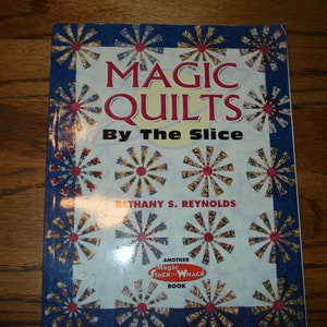 May include: Book cover with a blue background and a white title that reads "Magic Quilts By The Slice" with a red and white starburst pattern. The author's name is Bethany S. Reynolds. The book is part of the "Another Magic Stack & Whack Book" series.