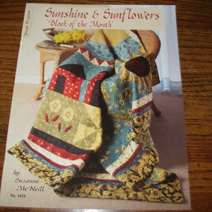 May include: A quilt pattern book featuring a quilt with a sunflower and sunshine theme. The book cover shows a quilt draped over a wicker chair. The title of the book is "Sunshine & Sunflowers" and "Block of the Month". The book is by Suzanne Me Neill and the number is 3424.