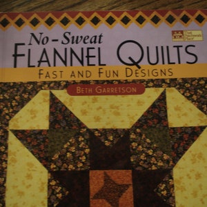 May include: Book cover with a purple background and the title "No-Sweat Flannel Quilts: Fast and Fun Designs" by Beth Garretson. The cover features a quilt design with a star in the center and a floral pattern.