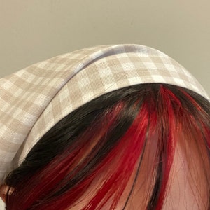 Pu&ograve; includere: Un cerchietto per capelli in tessuto a quadri beige e bianco.