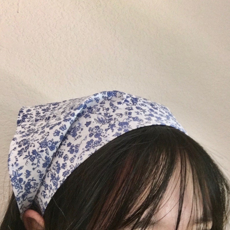 Pu&ograve; includere: Un bandana bianco con un motivo floreale blu legato intorno alla testa di una persona.