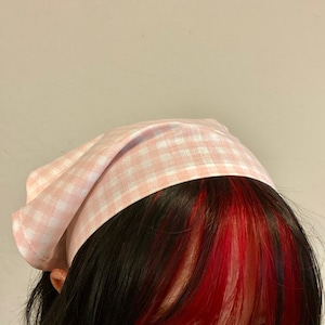 Pu&ograve; includere: Un bandana a quadri rosa e bianco legato intorno alla testa di una persona.