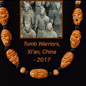 May include: A necklace made of dark brown wooden beads carved into the shape of human faces. The beads are interspersed with black beads. The necklace is displayed against a black background. A small photo of the Terracotta Army in Xi'an, China is included in the image. The text "Tomb Warriors, Xi'an, China - 2017" is also included in the image.