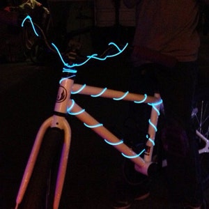 May include: A white bicycle frame with blue LED lights wrapped around it. The bike has a white handlebar and a black seat.