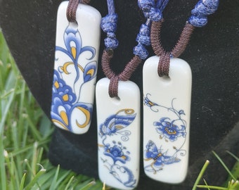 May include: Three porcelain pendants with blue and gold floral designs hang from blue cords. The pendants are rectangular and feature intricate floral patterns with butterflies.