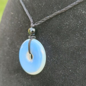 May include: A blue and white opal pendant necklace with a black cord. The pendant is a round disc with a hole in the center.