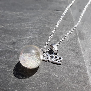 May include: A silver necklace with a clear glass orb pendant filled with iridescent glitter and a silver charm with the year 2022.