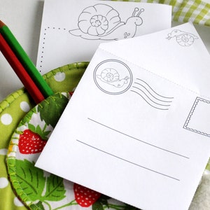 Puede incluir: Un sobre blanco con un dise&ntilde;o de caracol y un espacio en blanco para escribir un mensaje. El sobre tiene un sello con un dise&ntilde;o de caracol y un espacio en blanco para un sello. El sobre est&aacute; sobre una tela verde y blanca con lunares blancos.