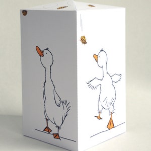 May include: A white paper craft with a goose on each side. The goose on the left is looking up and the goose on the right is looking to the side. Both geese have orange beaks and feet.