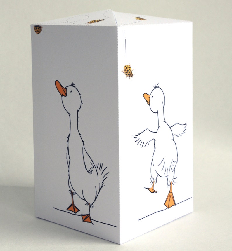 May include: A white paper craft with a goose on each side. The goose on the left is looking up and the goose on the right is looking to the side. Both geese have orange beaks and feet.