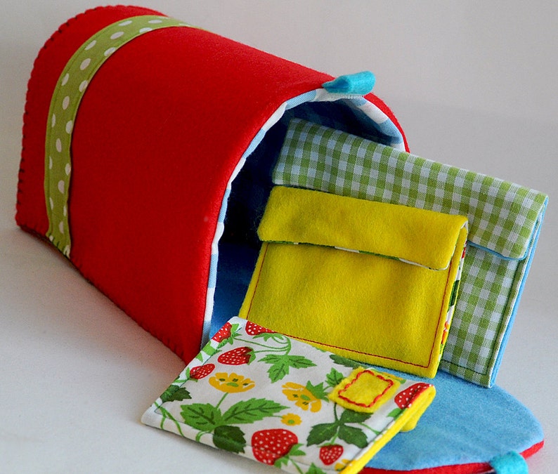 Puede incluir: Un buz&oacute;n de fieltro rojo con una cinta de lunares verde y blanco. El buz&oacute;n est&aacute; abierto y tiene varios sobres de fieltro de colores en su interior.