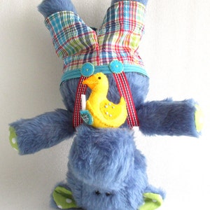May include: A blue plush toy elephant wearing plaid overalls and a yellow rubber ducky. The elephant is standing on its head with its arms and legs outstretched.