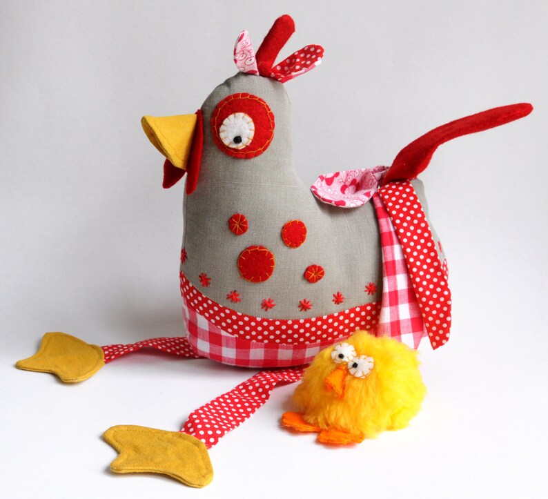 May include: A gray fabric chicken with red and white polka dot accents and a yellow beak. The chicken has a red tail and is holding a yellow chick with a fluffy yellow body.