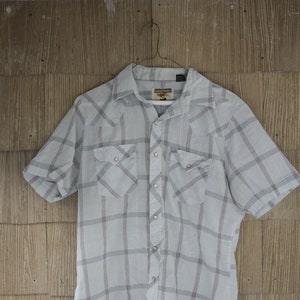 May include: A light blue and white plaid short-sleeved button-down shirt with two chest pockets. The shirt has a label that reads "Buffalo David Bitton".