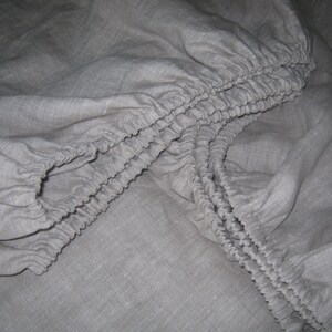 May include: A close-up of a gray fitted sheet with elastic edging. The sheet is made of a soft, natural fabric.
