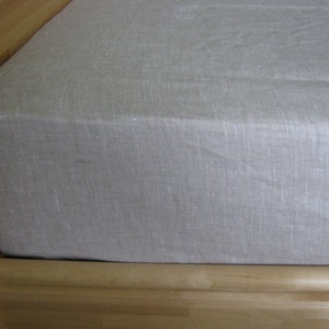 Oatmeal linen fitted sheet on a mattress on a pine bed frame, corner view