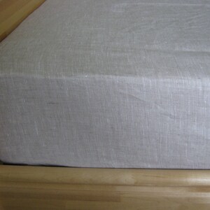 May include: A white linen fitted sheet for a bed. The sheet is made of a natural fabric and has a smooth, even texture.