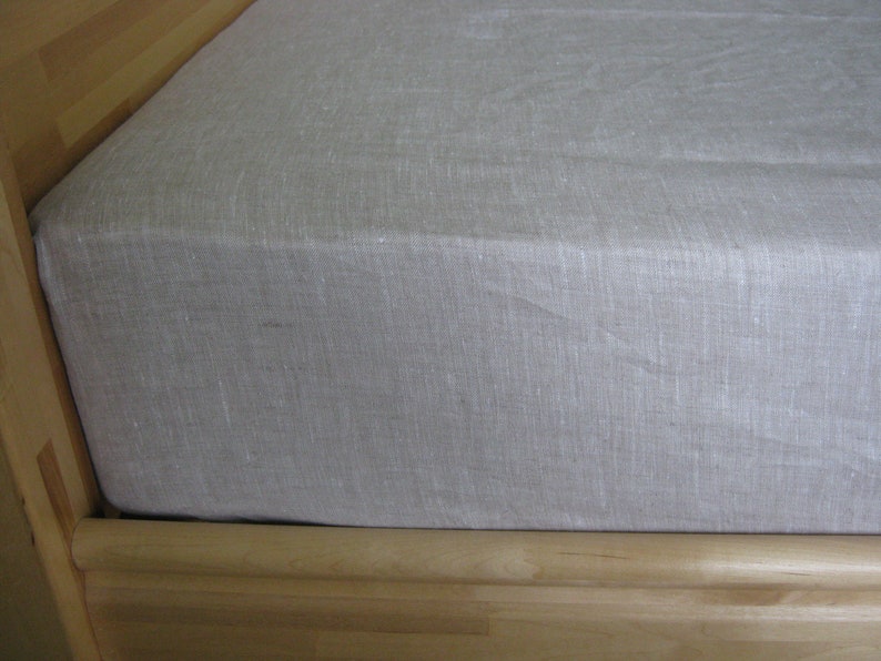 May include: A white linen fitted sheet for a bed. The sheet is made of a natural fabric and has a smooth, even texture.