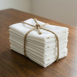 Large stack of white linen napkins tied with twine on a wooden table