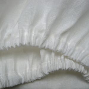 May include: White cotton fabric with a gathered, ruffled edge. The fabric is soft and has a slightly textured surface.