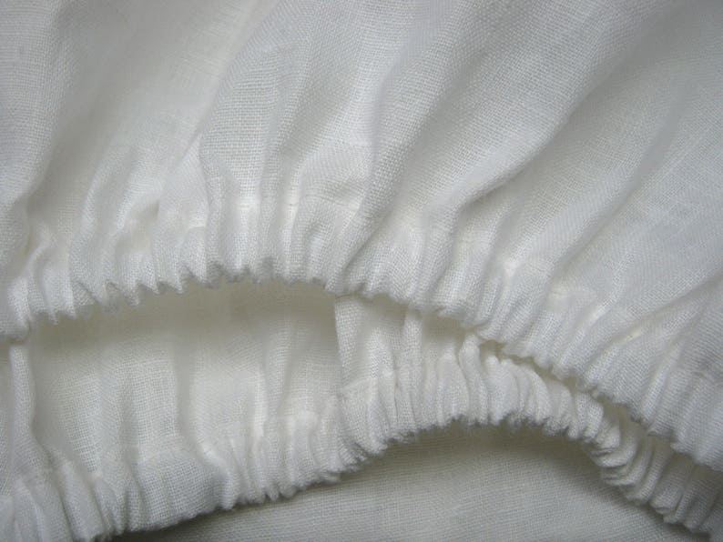 May include: White cotton fabric with a gathered, ruffled edge. The fabric is soft and has a slightly textured surface.