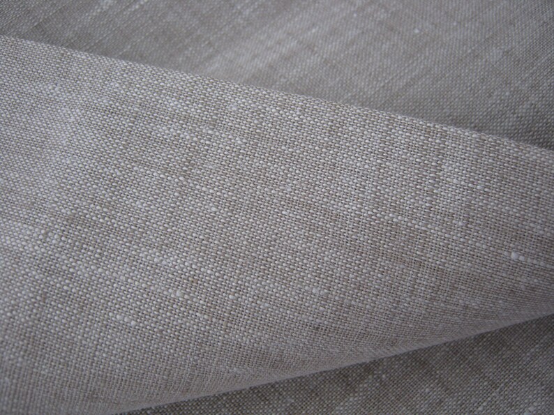 Op de afbeelding: Close-up van een natuurlijke linnen stof met een textuur geweven. De stof is licht beige van kleur en heeft een licht ruw gevoel.