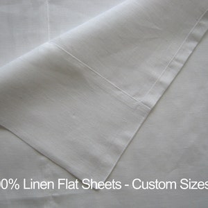 Può includere: Un lenzuolo piatto in lino bianco al 100%. Il lenzuolo è piegato a metà e i bordi sono visibili. Il testo "100% Linen Flat Sheets - Custom Sizes" è stampato nella parte inferiore dell'immagine.