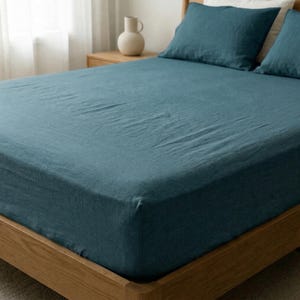 Dark teal linen fitted sheet and pillowcases on a deep mattress, corner view