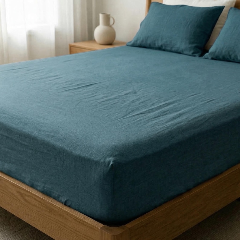 Dark teal linen fitted sheet and pillowcases on a deep mattress, corner view