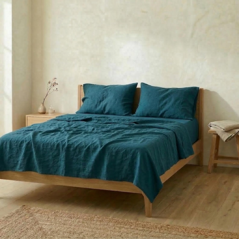 Bed with dark teal linen sheets and pillowcases in a room with a plaster wall