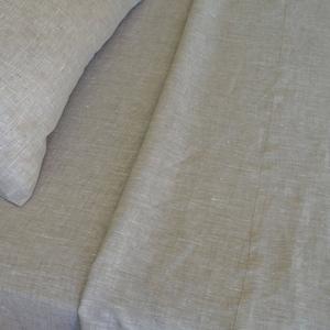 May include: A close-up of a gray linen bed sheet with a subtle texture. The sheet is folded in half, with the top half folded over the bottom half. The sheet is smooth and wrinkle-free.