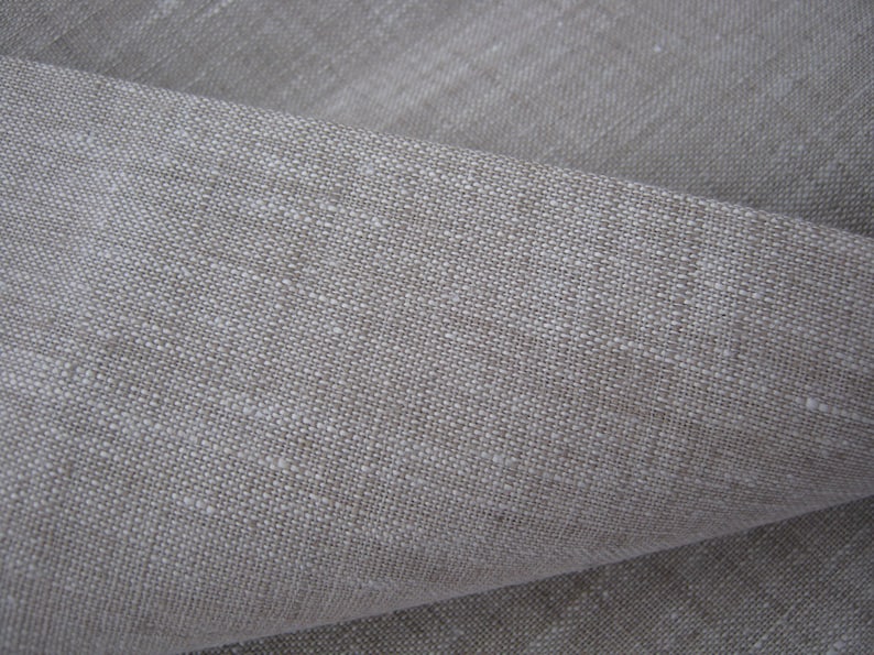 May include: Close-up of a natural linen fabric with a textured weave. The fabric is a light beige color and has a slightly rough feel.