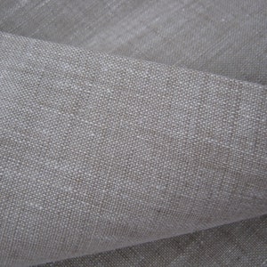 May include: Close-up of a natural linen fabric with a textured weave. The fabric is a light beige color.