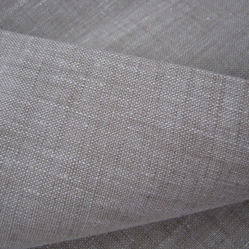 May include: Close-up of a natural linen fabric with a textured weave. The fabric is a light beige color.