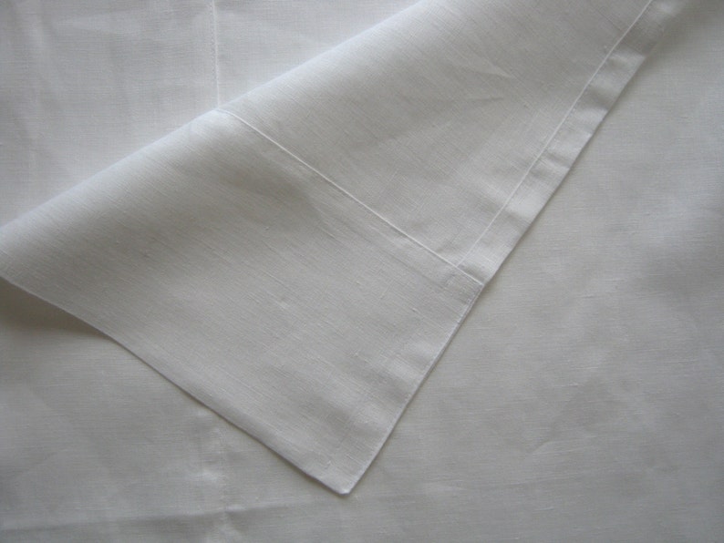 May include: A white linen tablecloth with a folded corner. The fabric is smooth and has a subtle texture.
