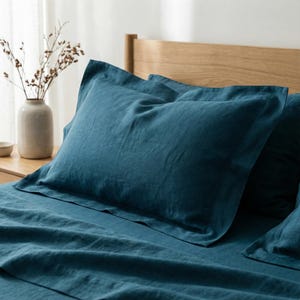 May include: A deep teal pillowcase with a wide flange border, crafted from a textured fabric. The pillowcase is positioned on a matching teal bed sheet, creating a cohesive bedding set with a visible weave pattern throughout the material.