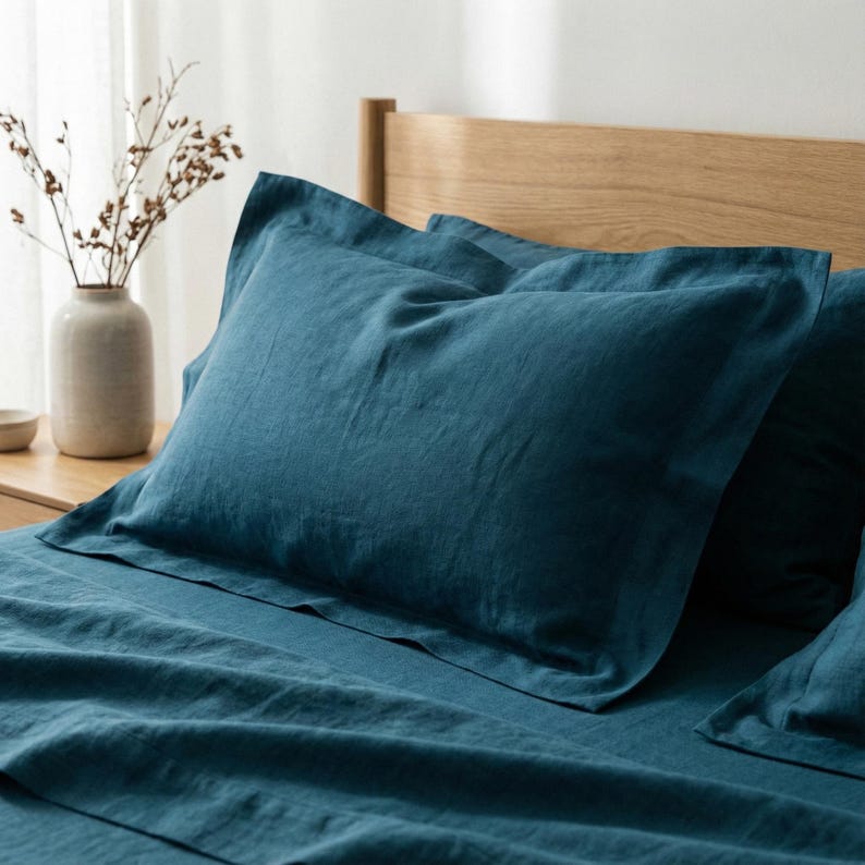 May include: A deep teal pillowcase with a wide flange border, crafted from a textured fabric. The pillowcase is positioned on a matching teal bed sheet, creating a cohesive bedding set with a visible weave pattern throughout the material.