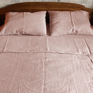 May include: A dusty rose linen bedding set with a flat sheet, fitted sheet, and two pillowcases. The bedding is made of a soft, natural fabric and has a relaxed, casual look.