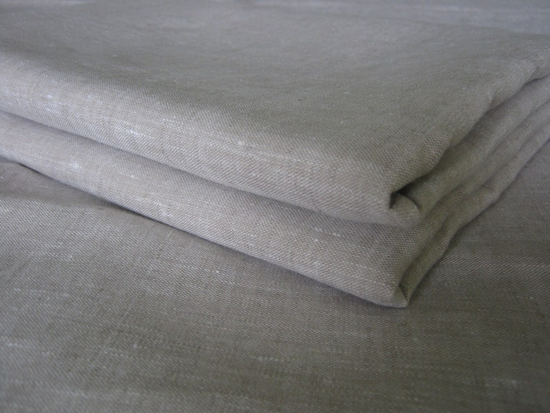 May include: A close-up of a folded piece of light gray linen fabric. The fabric has a subtle texture and a slightly wrinkled appearance.