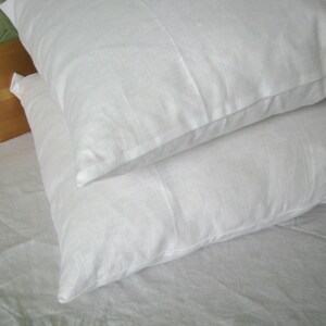 May include: Two white pillowcases on a white bed sheet. The pillowcases are made of a soft, smooth fabric.