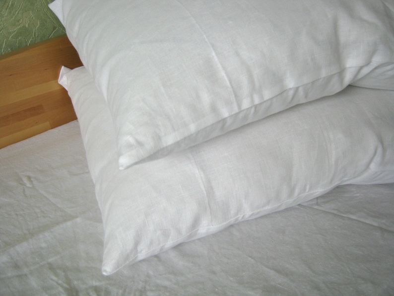 May include: Two white pillowcases on a white bed sheet. The pillowcases are made of a soft, smooth fabric.