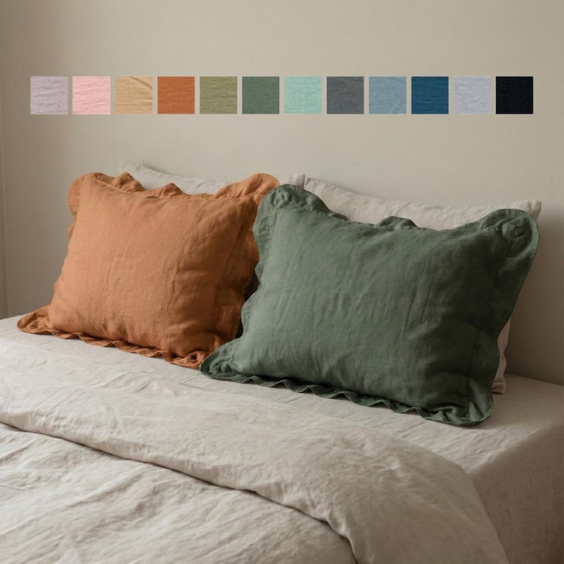 Puede incluir: Dos fundas de almohada rectangulares de lino con bordes de volantes, una en color naranja terracota c&aacute;lido y la otra en verde oliva apagado. Sobre las almohadas, una fila horizontal de doce peque&ntilde;as muestras cuadradas exhibe varios tonos.