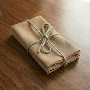 Stack of soft peach stonewashed linen napkins tied with twine on a wooden table