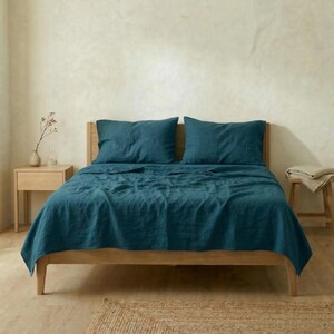 Bed made up in dark teal linen sheets and pillowcases on an oak bed frame