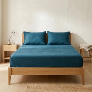 Dark teal linen fitted sheet and pillowcases on an oak bed, front view