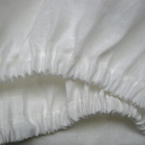 May include: Close-up of a white linen fabric with a gathered edge. The fabric is soft and textured, with a subtle sheen.