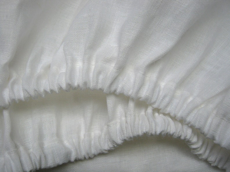 May include: Close-up of a white linen fabric with a gathered edge. The fabric is soft and textured, with a subtle sheen.