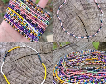 May include: A collection of beaded jewelry, including bracelets and necklaces, in various colors. The bracelets are stacked, showcasing a multitude of hues. Necklaces feature pink, blue, yellow, and white beads. The jewelry is displayed on a wooden surface.