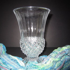 May include: A clear glass vase with a diamond pattern. The vase has a wide mouth and a narrow base. It is sitting on a blue and green patterned fabric.