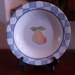 May include: A white ceramic soup bowl with a blue and white checkered border. The bowl features a painted image of a pear with green leaves.